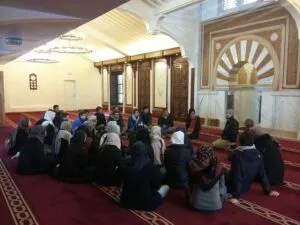 Grupo de estudiantes sentados en la alfombra de la sala de oración escuchando a un guía