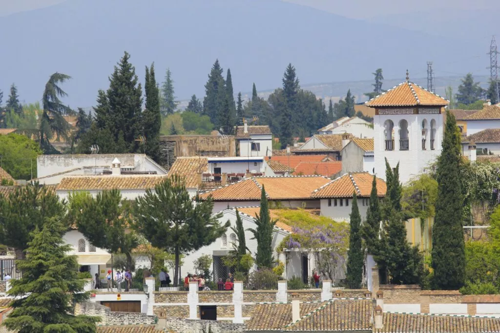 El alminar blanco de la mezquita entre los tejados y cipreses del Albaicín, con la sierra al fondo