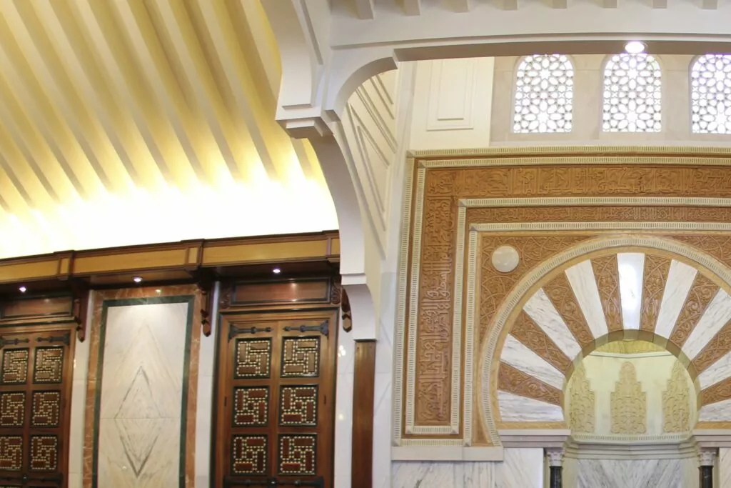 Mosque interior detail: golden slatted ceiling, inlaid wooden doors and the mihrab arch