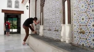 A man performing wudu at the row of taps in the mosque, under the blue geometric tilework