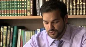 Hombre con camisa de rayas y corbata lee unos papeles ante una estantería de libros