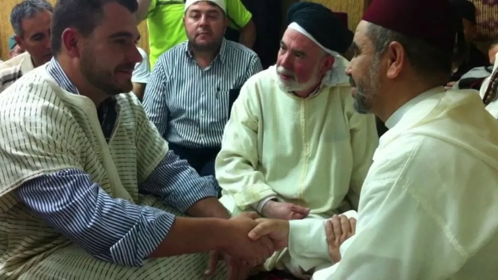 Joven estrechando la mano del imam durante la shahada, rodeado de la comunidad