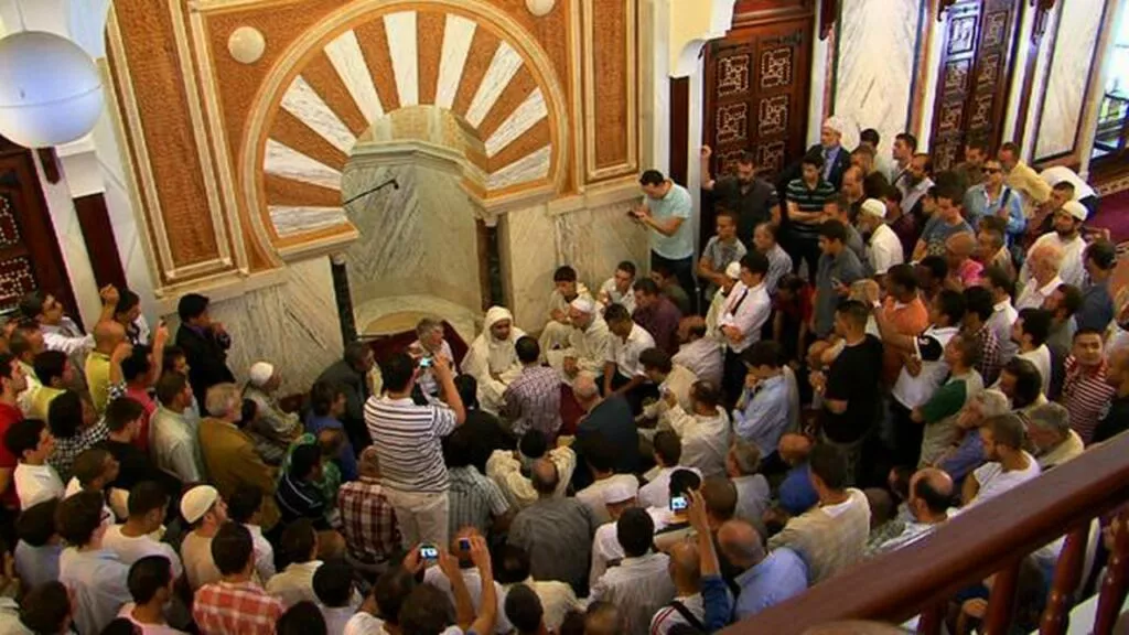 Sala de la mezquita abarrotada con gente de pie y sentada fotografiando junto al mihrab