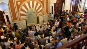 Sala de la mezquita abarrotada con gente de pie y sentada fotografiando junto al mihrab