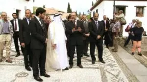 Sheij Sultan bin Muhammad Al Qasimi, con túnica blanca, llega acompañado a una plaza empedrada
