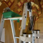 Escalera de pintor con pinceles y botes atados, ante el techo de mocárabes de madera pintada del zaguán