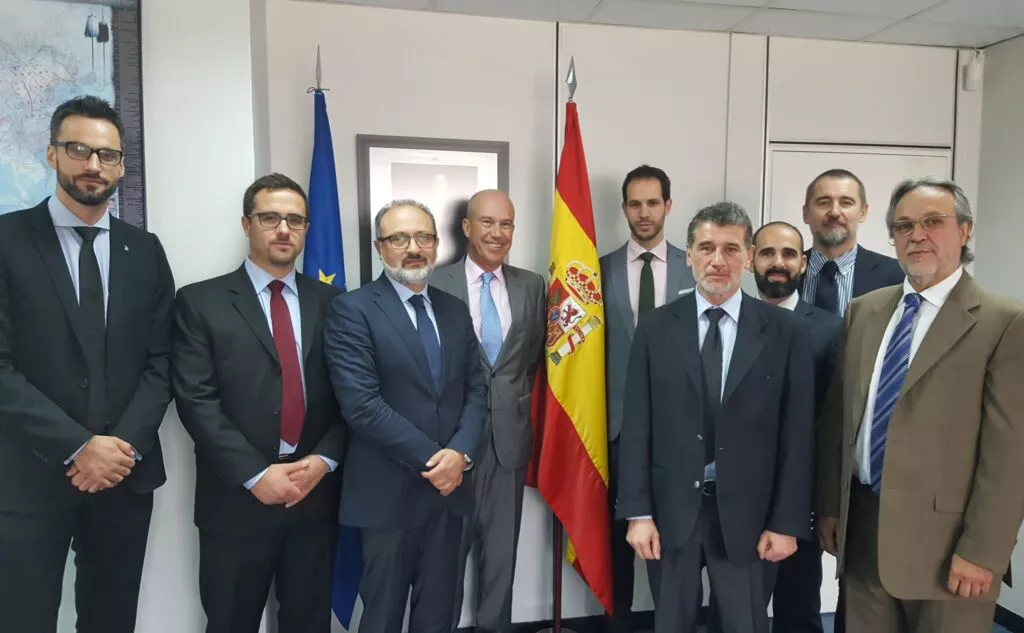 Nueve hombres con traje posan en un despacho junto a las banderas de España y de la Unión Europea