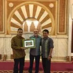 Tres hombres sostienen una fotografía enmarcada de la mezquita ante el mihrab de la sala de oración