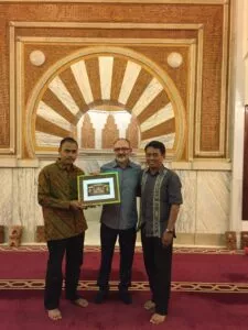 Tres hombres sostienen una fotografía enmarcada de la mezquita ante el mihrab de la sala de oración