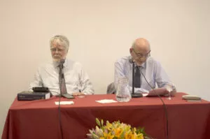 Dos ponentes ante los micrófonos en una mesa con mantel rojo y un libro sobre el Islam