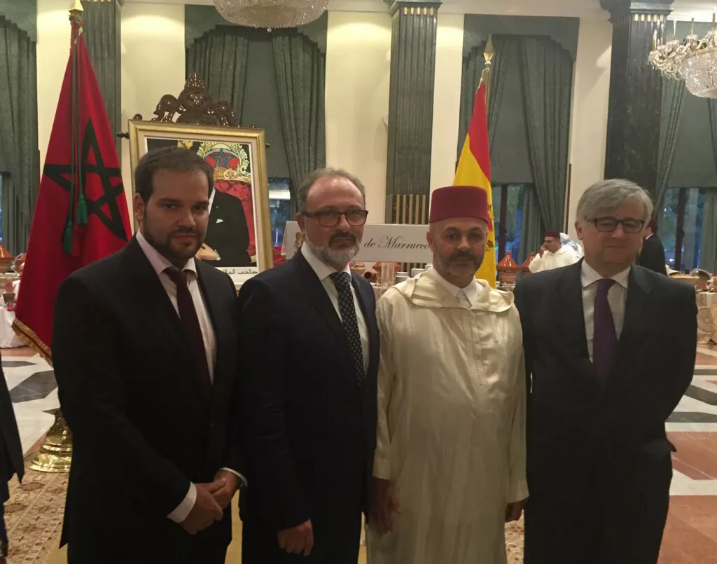 Cuatro invitados posan ante las banderas de Marruecos y España y el retrato del rey en la recepción