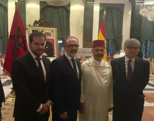 Cuatro invitados posan ante las banderas de Marruecos y España y el retrato del rey en la recepción