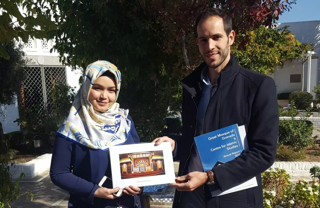 Visitante con pañuelo y un responsable de la Mezquita sostienen una lámina enmarcada del mihrab
