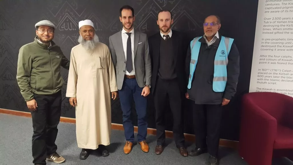 Cinco hombres posan ante un mural con caligrafía árabe y un panel sobre la kiswa de la Kaaba