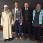 Cinco hombres posan ante un mural con caligrafía árabe y un panel sobre la kiswa de la Kaaba