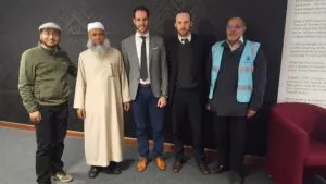 Cinco hombres posan ante un mural con caligrafía árabe y un panel sobre la kiswa de la Kaaba