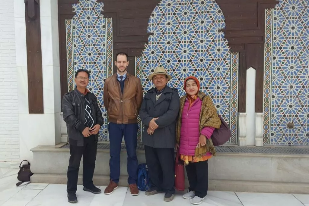 Indonesian visitors and a mosque representative in front of the blue tiled facade of the mosque