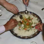 Varios comensales comparten con cuchara una fuente de arroz con verduras servida en el centro de la mesa