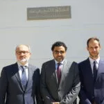 Tres hombres trajeados posan bajo la placa Mezquita Mayor de Granada en árabe y español
