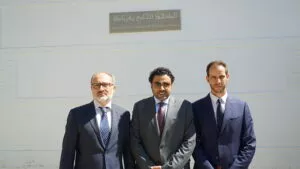 Tres hombres trajeados posan bajo la placa Mezquita Mayor de Granada en árabe y español
