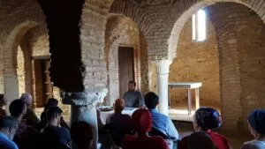 El conferenciante habla sentado a una mesa en una sala de arcos de herradura ante el público