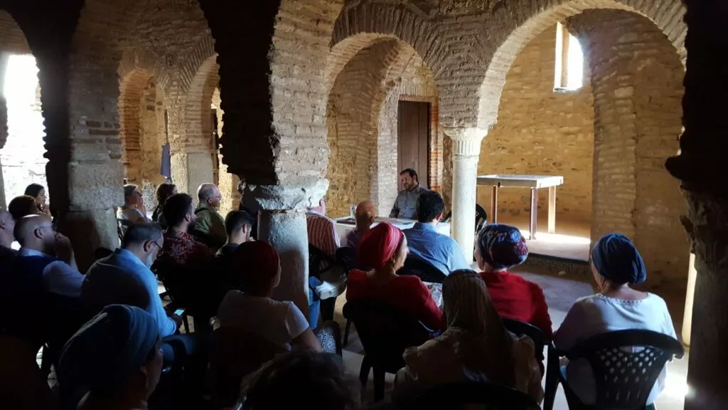 Charla en una sala de arcos de herradura de ladrillo con el ponente en la mesa y el público sentado