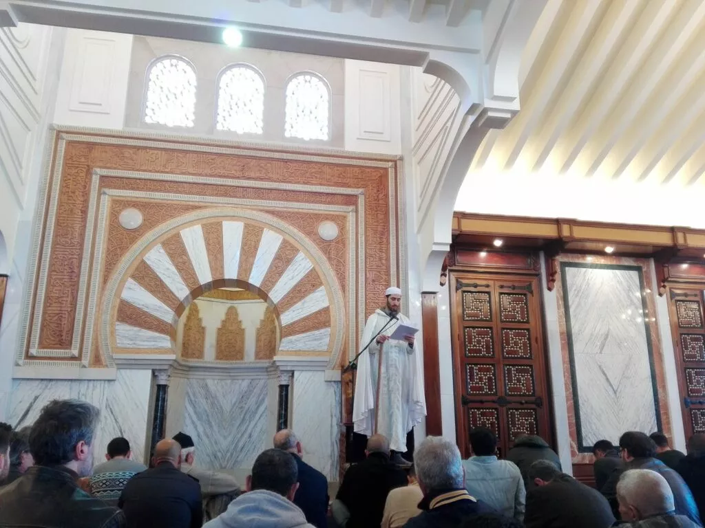 Predicador de blanco lee la jutba ante el mihrab mientras los fieles escuchan sentados
