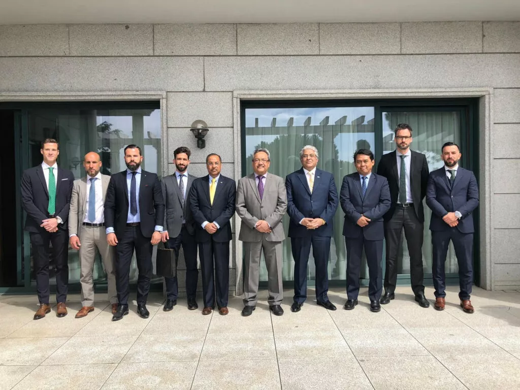 Diez hombres con traje posan en fila ante la fachada de granito de un edificio institucional