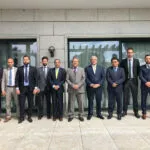 Diez hombres con traje posan en fila ante la fachada de granito de un edificio institucional