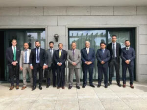Diez hombres con traje posan en fila ante la fachada de granito de un edificio institucional