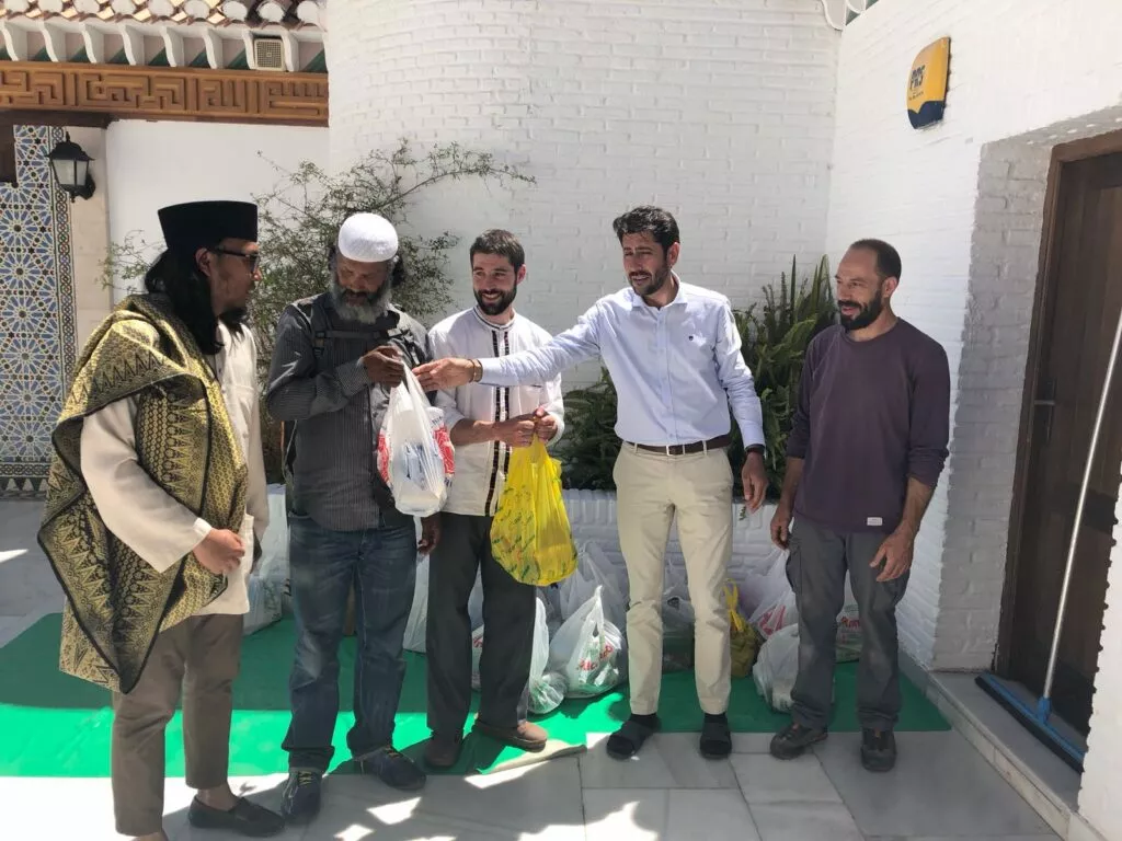 Cinco hombres en el patio de la mezquita entregando bolsas con alimentos sobre una estera verde