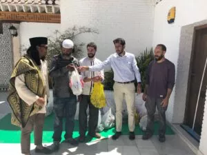 Cinco hombres en el patio de la mezquita entregando bolsas con alimentos sobre una estera verde