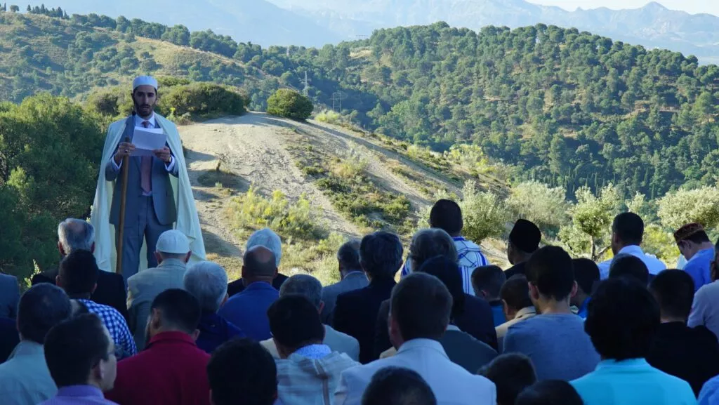 Jatib leyendo la jutba del Eid al aire libre ante los fieles, con los montes al fondo