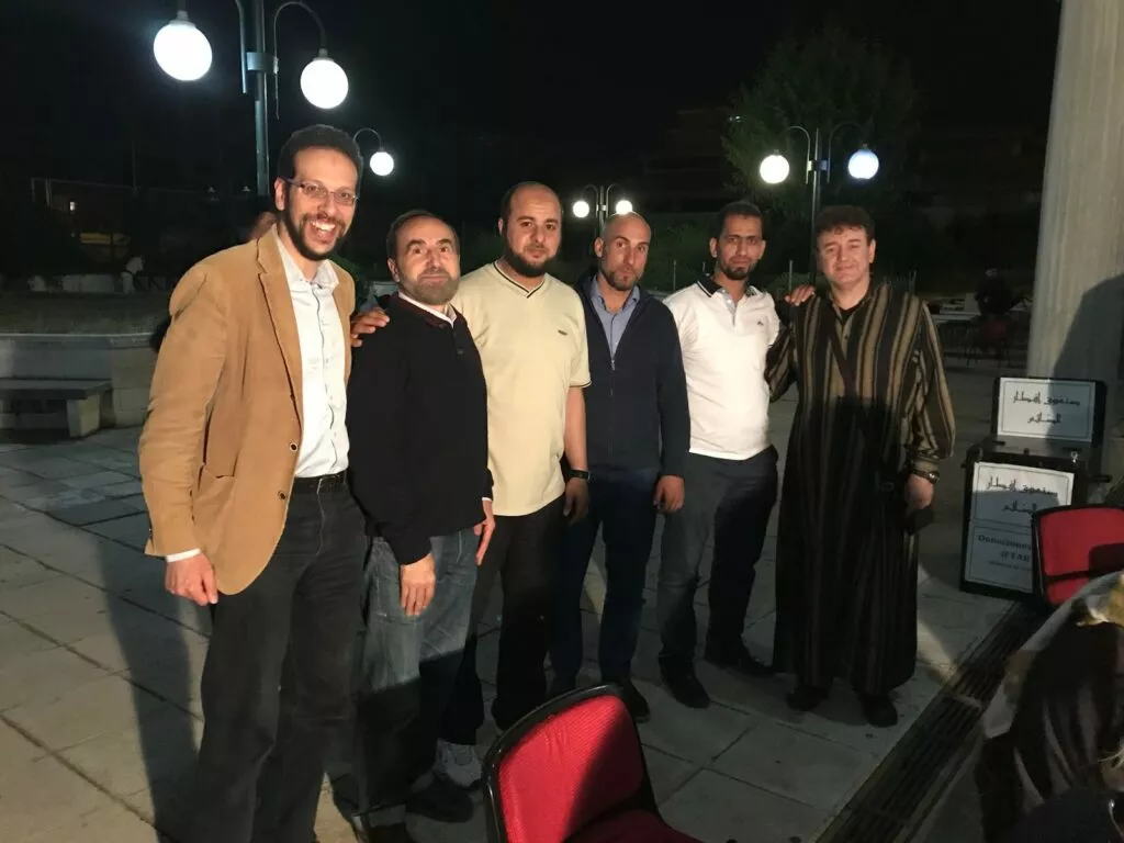 Seis hombres posan de noche en la explanada de una mezquita junto al cartel de donaciones del iftar