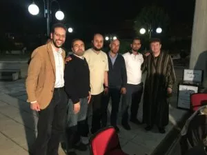 Seis hombres posan de noche en la explanada de una mezquita junto al cartel de donaciones del iftar