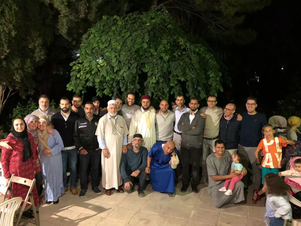 Hombres, mujeres y niños posando de noche en un jardín bajo un gran árbol