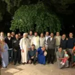 Hombres, mujeres y niños posando de noche en un jardín bajo un gran árbol