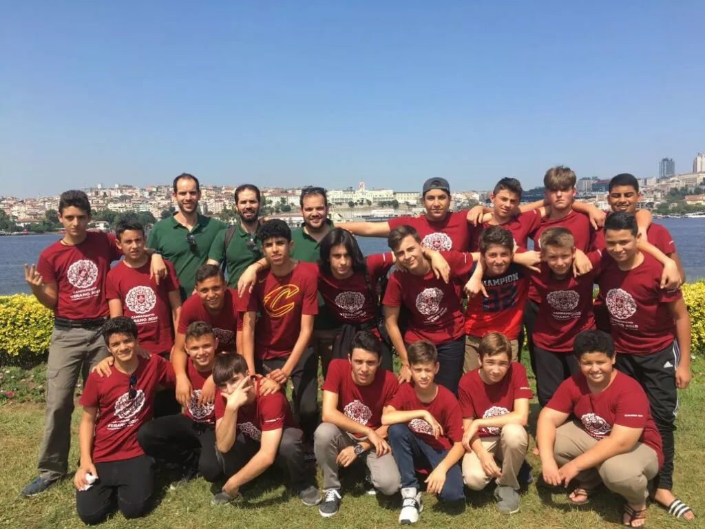 Grupo de adolescentes con camisetas granates de un campamento posando en el césped junto a una ría