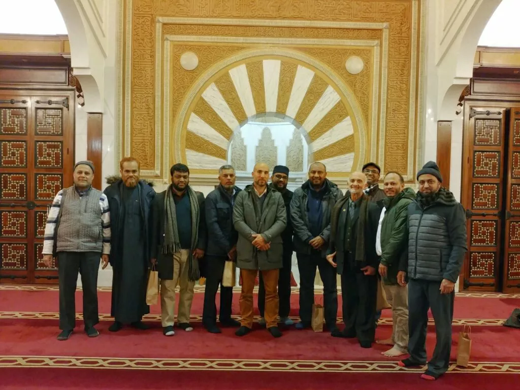 Doce hombres posan sobre la alfombra roja ante el mihrab dorado de una mezquita