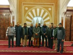 Doce hombres posan sobre la alfombra roja ante el mihrab dorado de una mezquita