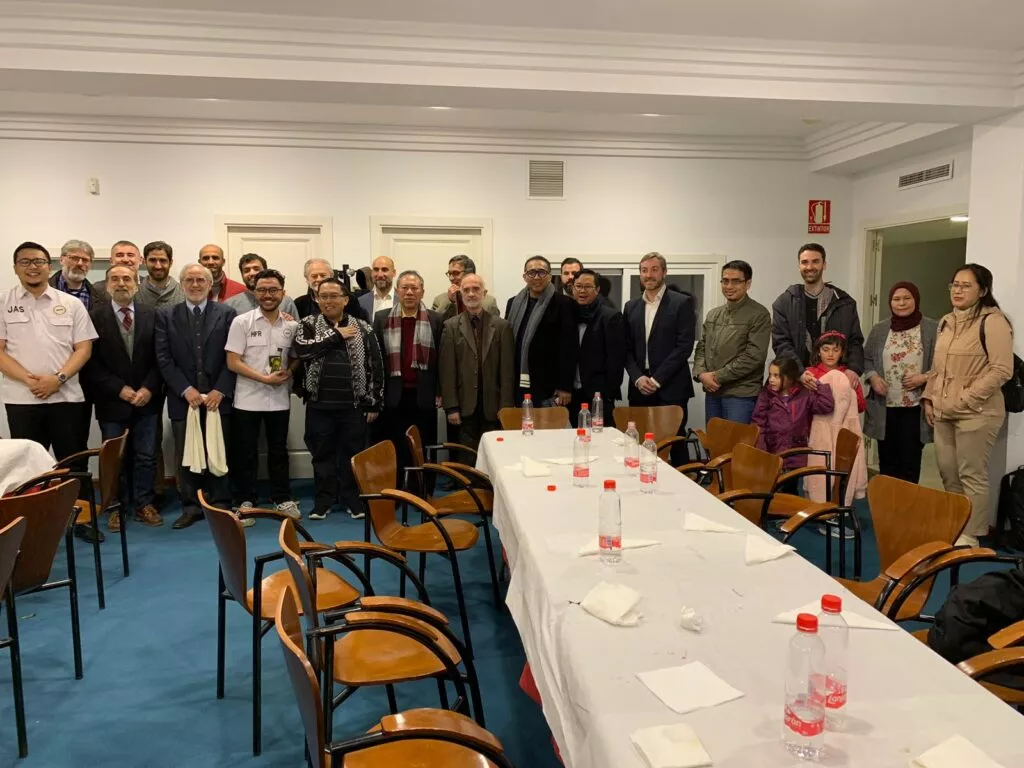Grupo numeroso, con mujeres y niñas, posa junto a la mesa larga aún puesta de una sala de reuniones