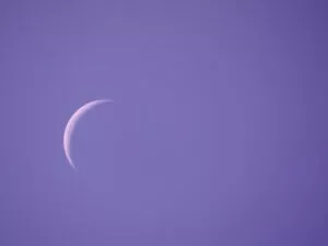 Fina luna creciente blanca recortada en un cielo violeta al anochecer