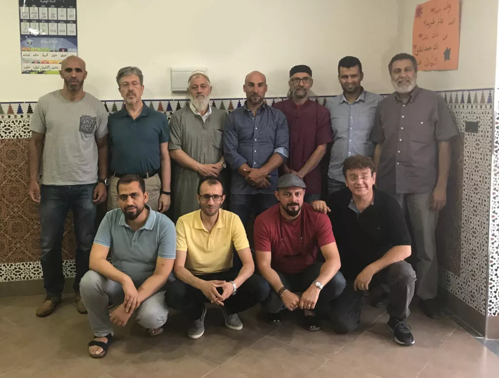Once hombres posan juntos en una sala con zócalo de alicatado y carteles en árabe en la pared