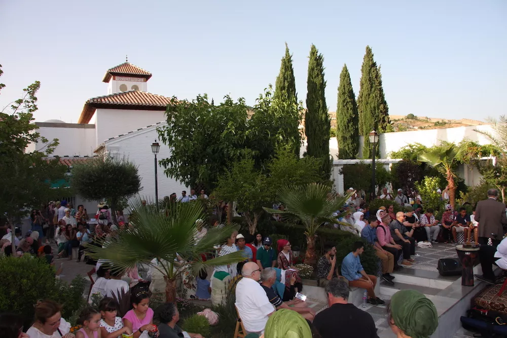 Encuentro al aire libre en el jardín de la mezquita al atardecer, con el público sentado entre las palmeras y el alminar al fondo