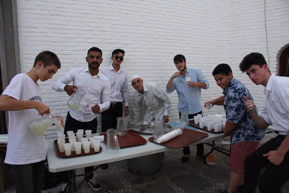Un grupo de voluntarios sirve vasos de bebida en las mesas del patio durante la fiesta