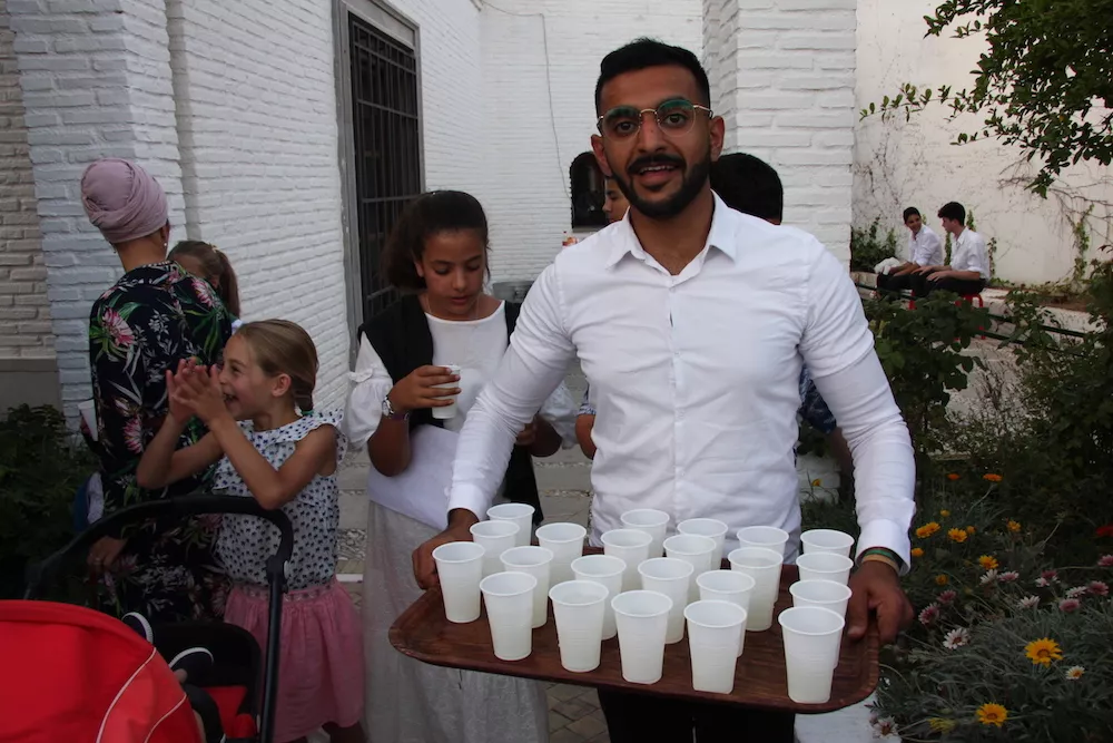 Un voluntario lleva una bandeja llena de vasos entre los asistentes en el patio