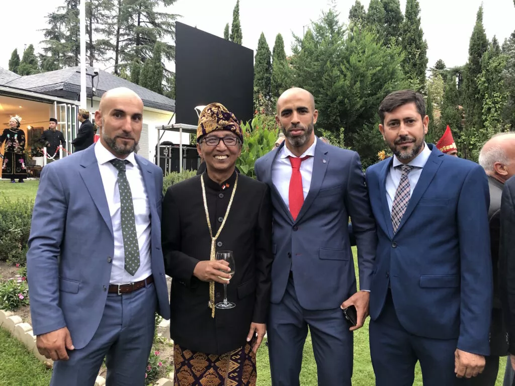 Tres hombres de traje posan en un jardín con un invitado vestido con traje tradicional indonesio