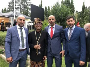 Tres hombres de traje posan en un jardín con un invitado vestido con traje tradicional indonesio