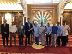 Grupo de hombres posa descalzo ante el mihrab de la sala de oración, sobre la alfombra roja