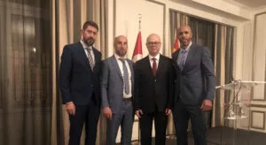 Cuatro hombres de traje posan ante las banderas de Turquía y España en un salón de recepciones